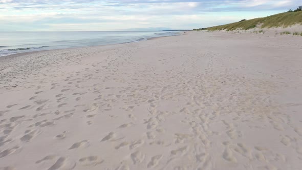 AERIAL: Very Slow Flying Above Sandy Beach with Foot Prints and Seashore on the Side