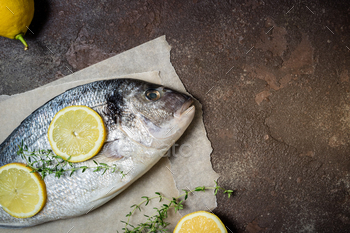 Fresh raw fish closeup. Dorado fish with lemon and thyme on kitchen table. Cooking fish / Photodune, Misc