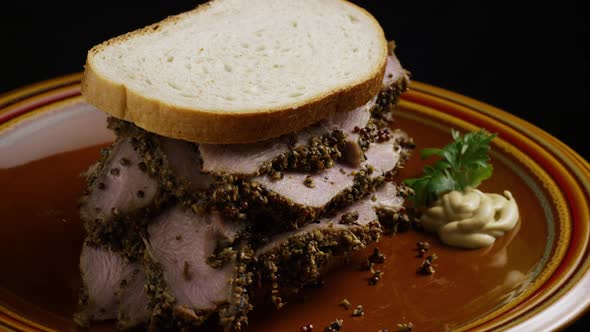 Rotating shot of delicious, premium pastrami sandwich next to a dollop of dijon mustard 