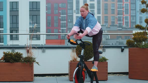 Athletic Girl Performing Aerobic Riding Training Exercises on Cycling Stationary Bike on House Roof