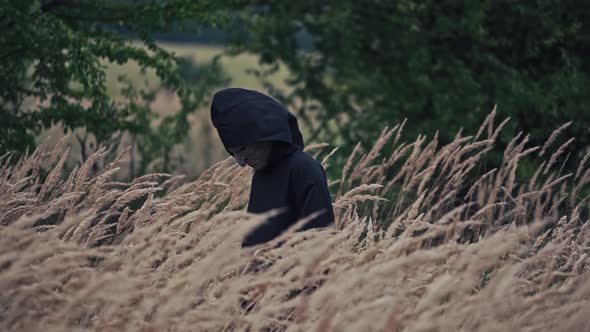 Dark ghost in black cloak with hood among nature