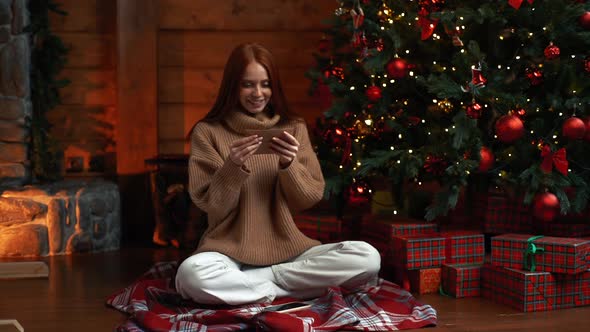 Happy Young Woman Getting Christmas Greeting Card From Her Beloved on Background of Xmas Tree