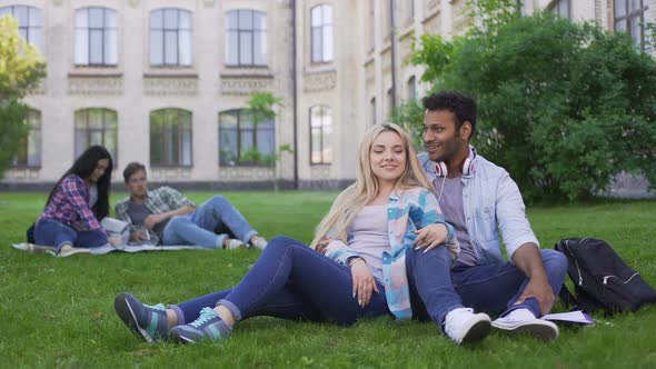 Multiracial Couple Relaxing on Grass, Talking and Smiling, First Love, Students