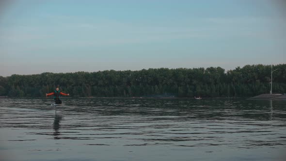 Man Riding a Hydrofoil Surfboard on Large Lake at Golden Sunset Sitting on Knees