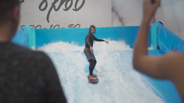 Teenager is Riding Surf Board on Wave Simulator Indoors