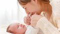 Closeup portrait of beautiful smiling mother kissing her baby's hands lying on bed against big - PhotoDune Item for Sale