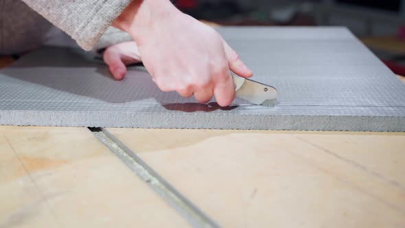 A Hand Cuts the Dense Gray Foam with a Clerical Knife