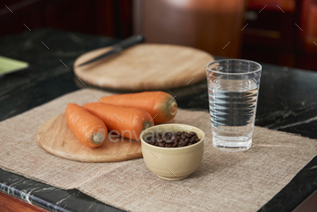 rrots on round-shaped cutting board, glass of water on napkin placed on kitchen table