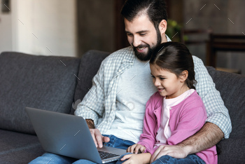 happy father with daughter sitting on couch and using laptop / Photodune, Misc