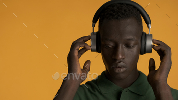 Handsome African American guy looking serious listening music in headphones over yellow background / Photodune, Misc