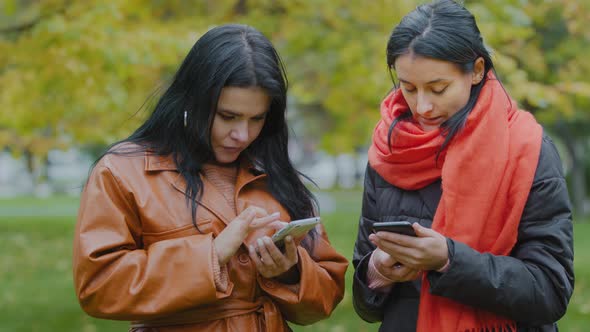 Two Young Women Holding Telephones in Hands Closeup Looking at Gadgets One Helps Other Download Cool