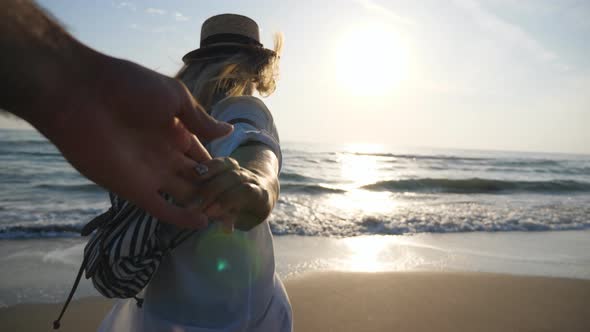 Follow Me Shot of Woman with Backpack Leading Her Boyfriend on Sea Shore at Sunset