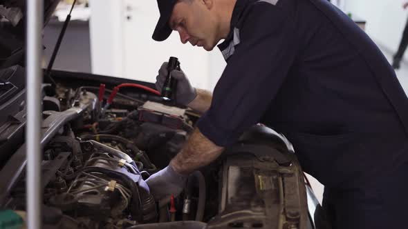 Car Service Worker Examinating Engine Under Hood with Flashlighter in Hand