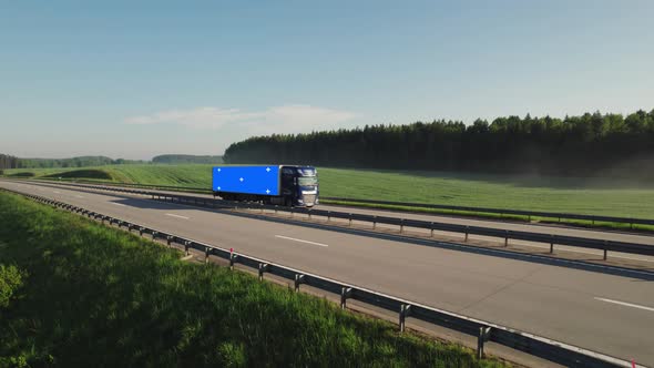 Large truck, the trailer of which shows a blue screen with markers for tracing, moves along a road.