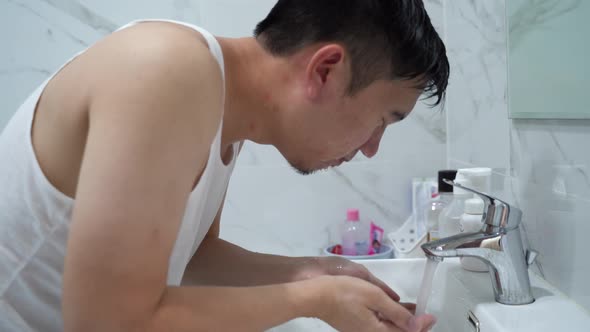 Young Guy Cleaning Face Above Sink in Bathroom