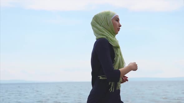 A Young Muslim Woman in a Burqa and Sports Sneakers Is Running Around the Sea