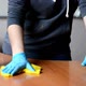 Girl in a Gray Sweater and Blue Gloves Washes a Wooden Table with a Yellow Rag - VideoHive Item for Sale
