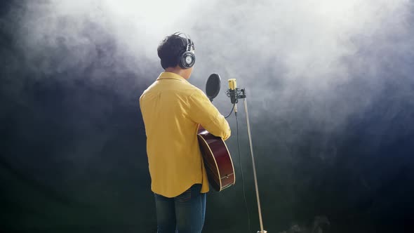 Young Boy With Headphone Playing A Guitar And Singing On The White Smoke Black Background