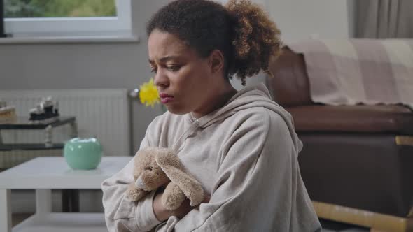 Sad Frustrated African American Woman Sitting at Home Hugging Toy Rabbit