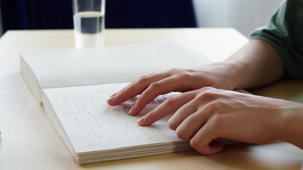 Blind Person Reading Braille Book Touching Letters on Sheet of Paper Using His Fingers Sitting at