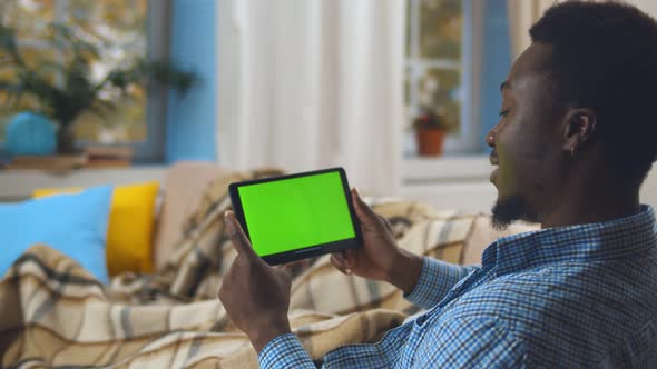 African Man with Tablet Computer Having Video Call and Resting on Couch at Home