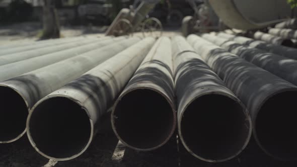 Metal Industrial Pipes Lying Under Sunlight with Heavy Machinery at the Background. Camera Moves