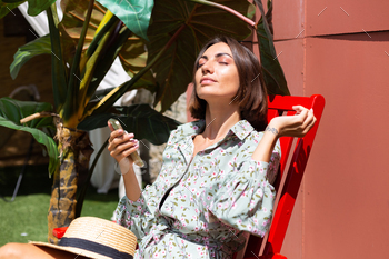 Beautiful woman in summer dress sits on chair in  backyard at sunny day with mobile  phone / Photodune, Misc