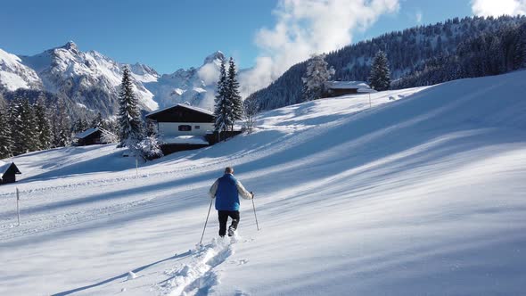 A man walking on a snow field with ski walking sticks, and mountain alps