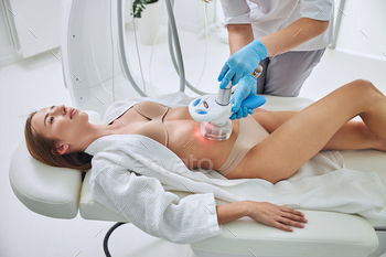 Charming adorable female lying on medicine table while getting cavitation body contouring treatment / Photodune, Misc