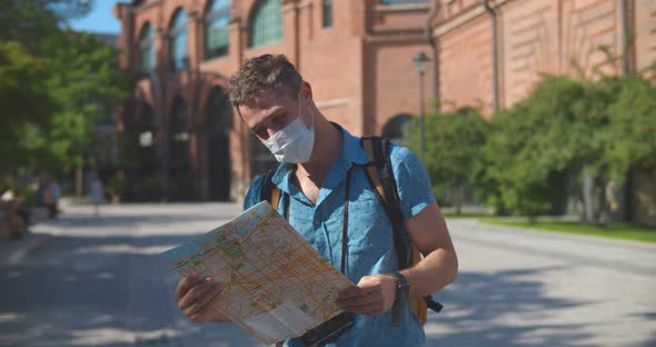 Young Caucasian Tourist Man in Safety Mask Looking for Directions on Map