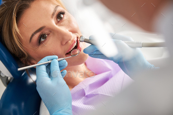 Dentist drilling tooth of a woman and using dental mirror / Photodune, Misc