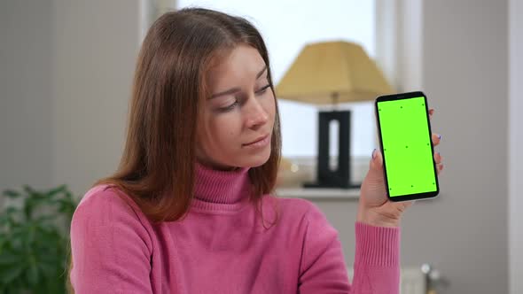 Confident Beautiful Caucasian Young Woman Posing with Green Screen Smartphone Indoors