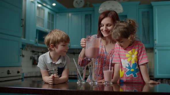 Happy family of mother and two kids drinking berry smoothie at home