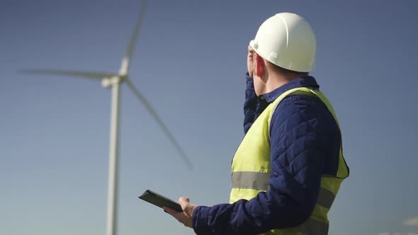 Specialist Standing Near Wind Mill and Entering Information Into