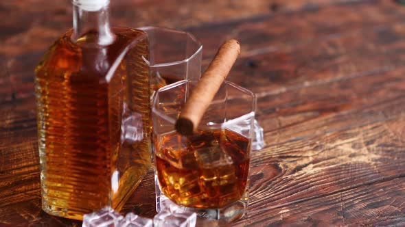 Bottle of Whiskey with Two Glasses and Cuban Cigar Placed on Rustic Wooden Table