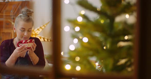 Woman Drinking Coffee At Home Seen Through Window