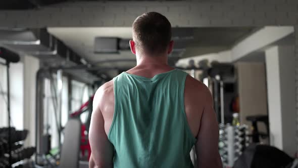 A man in a gym standing with his back raises a barbell in front of him