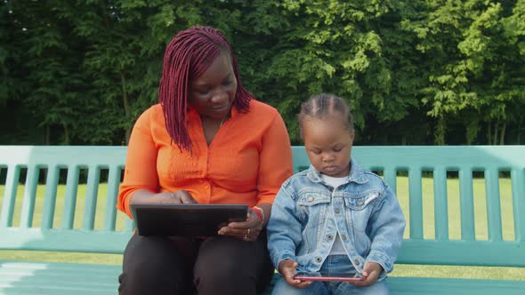 Pretty Black Mother and Toddler Girl Networking with Digital Devices on Park Bench