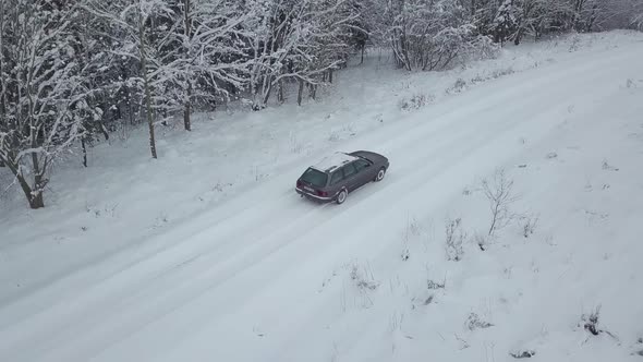 car is moving on winter road in forest. Shooting from drone down.