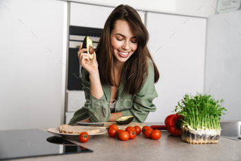 Cheerful beautiful woman showing avocado while making salad / Photodune, Misc