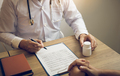 Confident doctor man holding a pill bottle and writing while talking with senior patient - PhotoDune Item for Sale