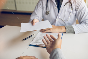 Asian male doctor talking in clinic room and handing a prescription to the patient. / Photodune, Misc