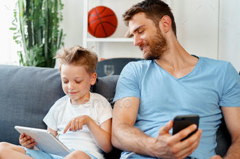 Little boy and his dad watching videos on digital tablet together sitting on sofa / Photodune, Misc