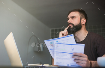 Bearded young man sitting at table looking at documents / Photodune, Misc