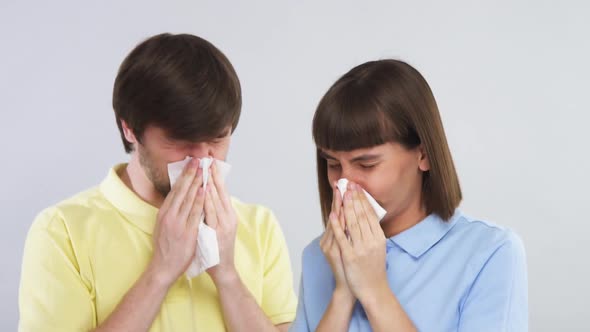 Young Couple in Yellow and Blue Shirt Blow Noses Into Tissues on Grey Background