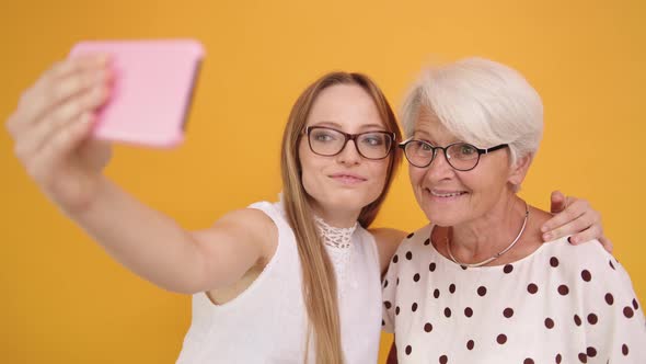 Senior and Young Woman Taking Selfies Isolated on Orange Background