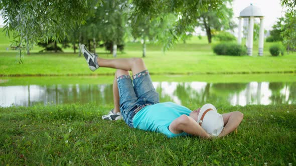 Young Man in a Hat Is Resting Lying on the Grass in a City Park