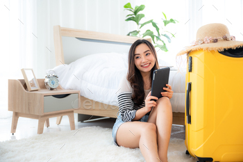 Happy asian young female selfie photo with smartphone, luggage, hat, swimming suit at the hotel bed