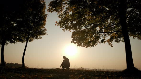 Against the Background of the Orange Sunset Sky Silhouettes of a Man Walking with a Dog During