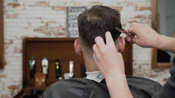 Barber Cutting Hair with Scissors to a Handsome Young Man